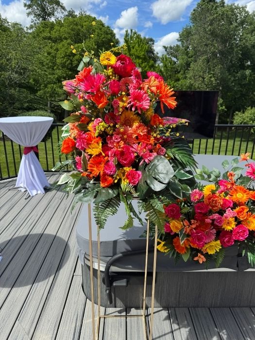 Tall floral stand filled with tropical greens and bold pink and orange blooms, available from Simply LaMayed for event rentals and displays.