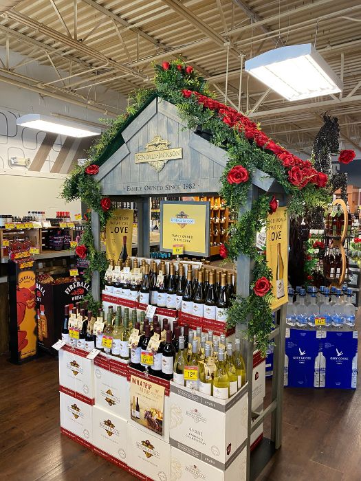 Full view of a Kendall-Jackson and La Crema wine display decorated with red roses, lush greenery, and custom florals created by Simply LaMayed for the Kentucky Derby 150th event.