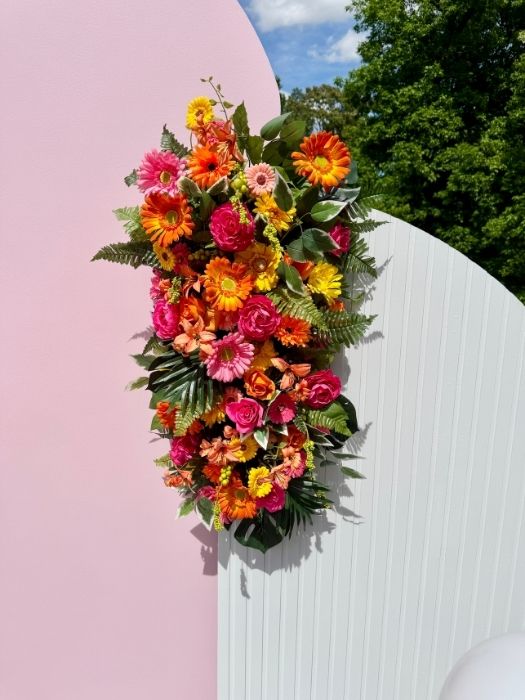 Colorful floral swag in hot pink and orange tones displayed on a curved pink and white wall backdrop by Simply LaMayed Custom Decor.