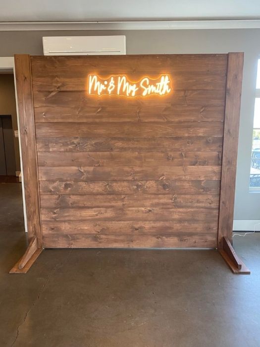 Rustic wood wall backdrop with custom neon 'Mr. and Mrs. Smith' sign, designed for weddings and receptions by Simply LaMayed Custom Decor.