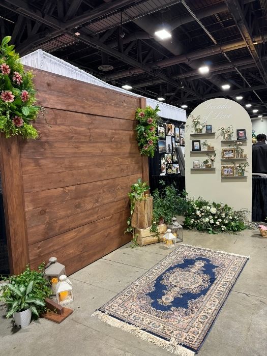 Wood backdrop paired with a cream arched photo wall featuring greenery and framed photos, styled by Simply LaMayed for an event showcase.